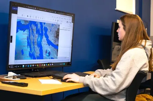 A Marine Science student looks at visualized data of coral reef maps on a large monitor